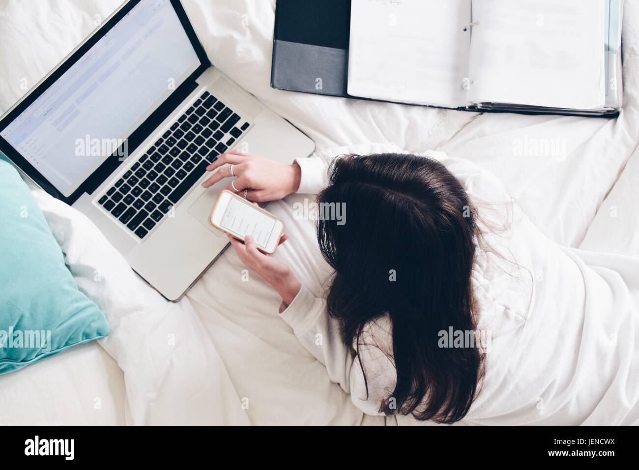 Adolescente acostado en la cama con su ordenador portátil y teléfono móvil Foto de stock