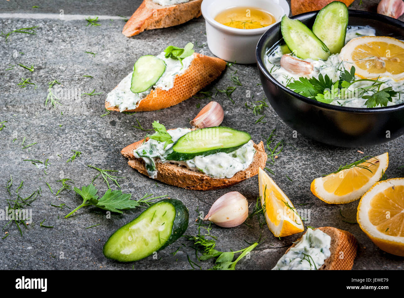 El Cáucaso y tradicional comida griega. Salsa tzatziki con ingredientes: pepino, eneldo, perejil, limón, ajo. Sobre una mesa de piedra oscura. Con sándwiches Foto de stock