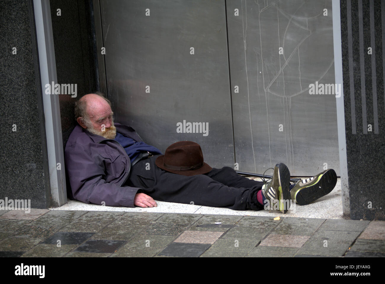 Mendicidad desempleados sin hogar hombre viejo anciano pensionista acostado en un pórtico con sombrero inapropiado Foto de stock