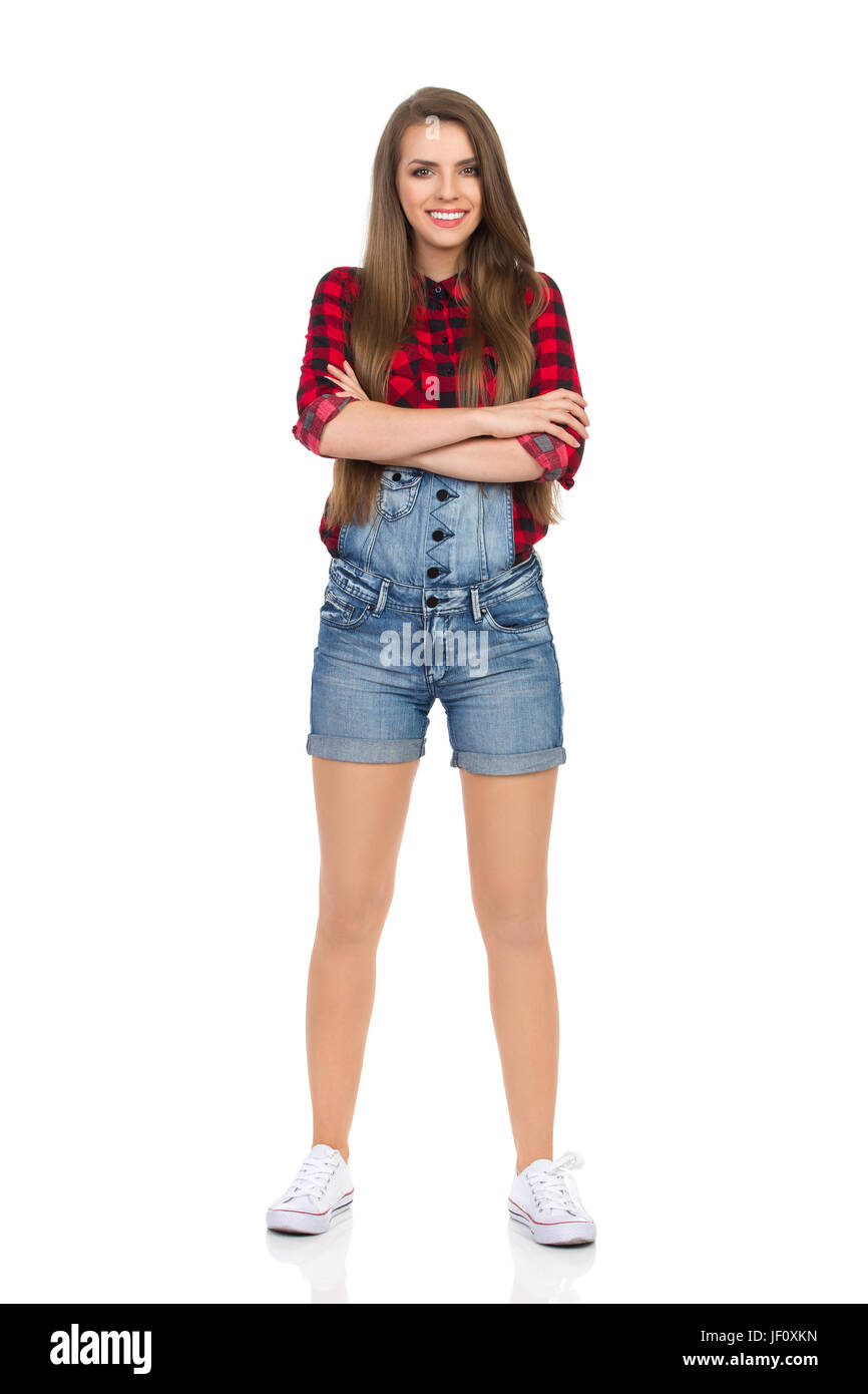 Mujer en rojo de leñadores de camisa, pantalones con peto shorts y zapatillas  blancas con los brazos cruzados. longitud completa foto de estudio aislado  en blanco Fotografía de stock - Alamy
