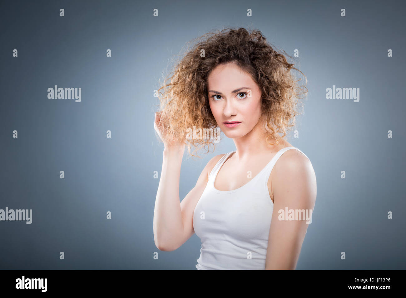 Retrato de una joven chica positiva tocando suavemente su cabello rizado. Natural, sana y auténtica de la mujer. Foto de stock