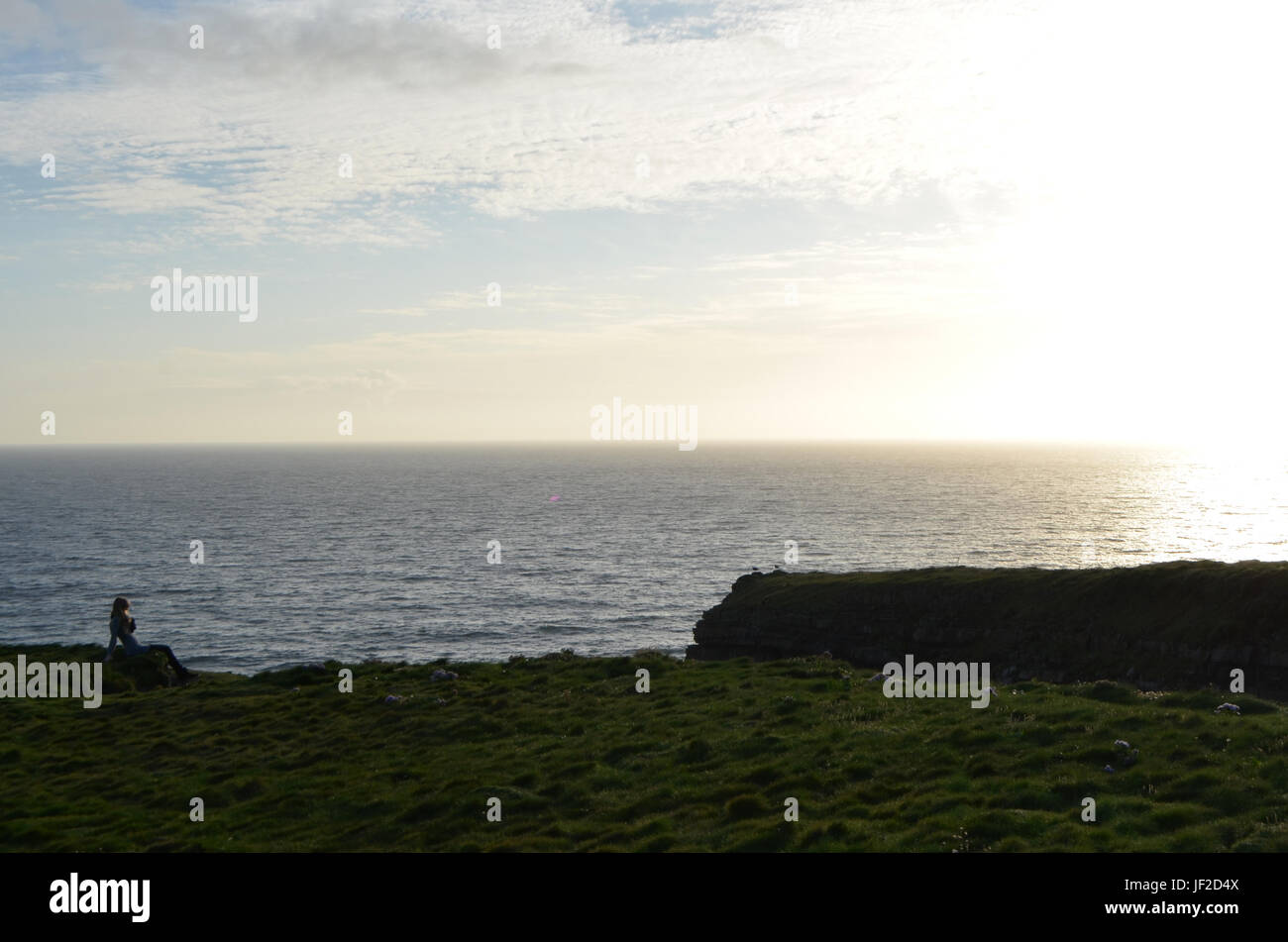 Mujer sentada en el borde del precipicio Vista de Loop Head Península en Clare, Irlanda Foto de stock
