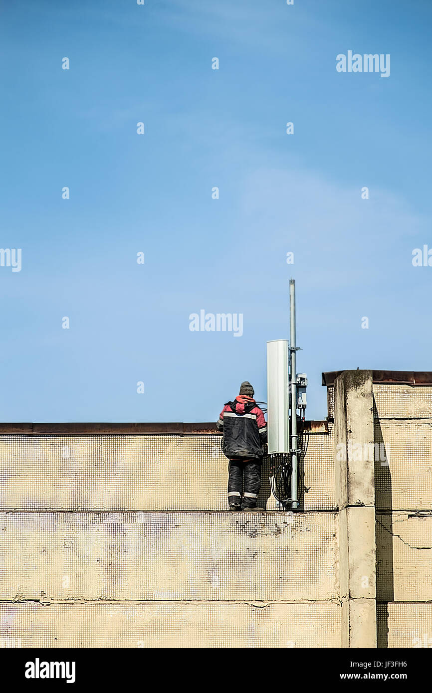 Un trabajador la fijación de una antena de radio móvil en la parte superior del edificio. Fondo de cielo azul Foto de stock