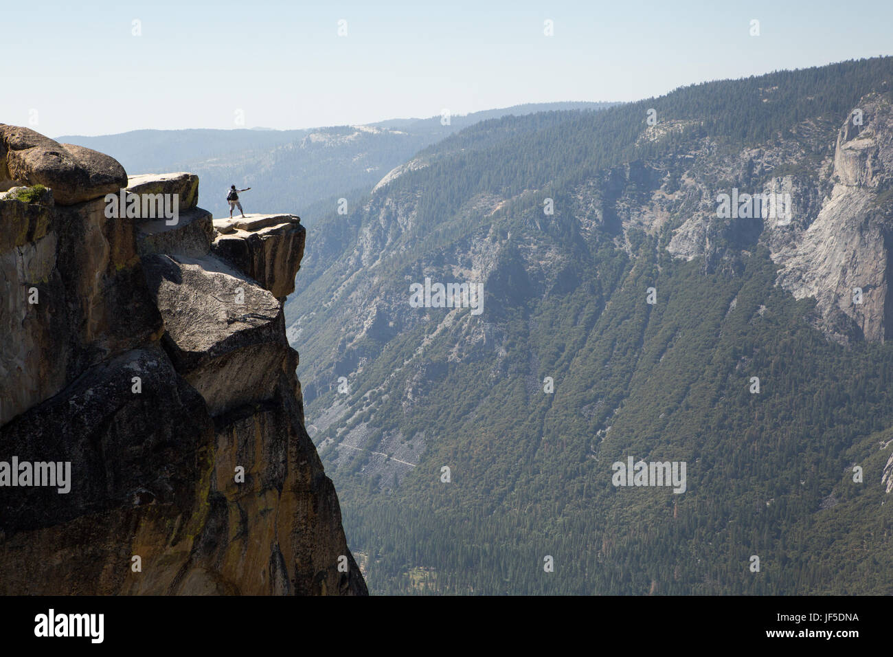 Un visitante al Parque Nacional de Yosemite se alza sobre una roca saliente en Taft Point. Esta cornisa, a una altitud de unos 7.500 pies, significa miles de pies por encima del Valle Yosemite. Foto de stock
