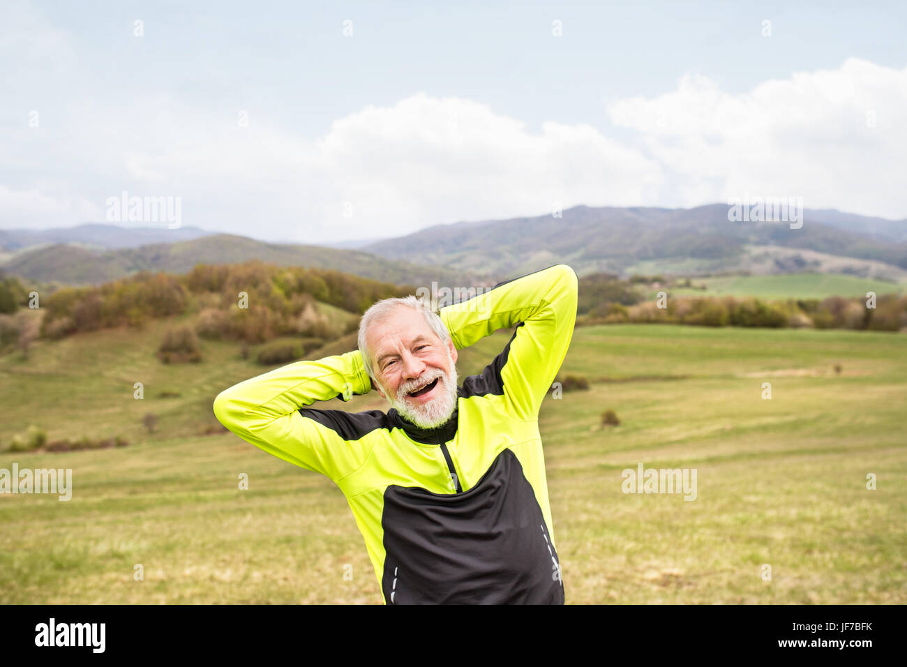 Senior activo corredor exterior en colinas verdes haciendo estiramientos. Foto de stock
