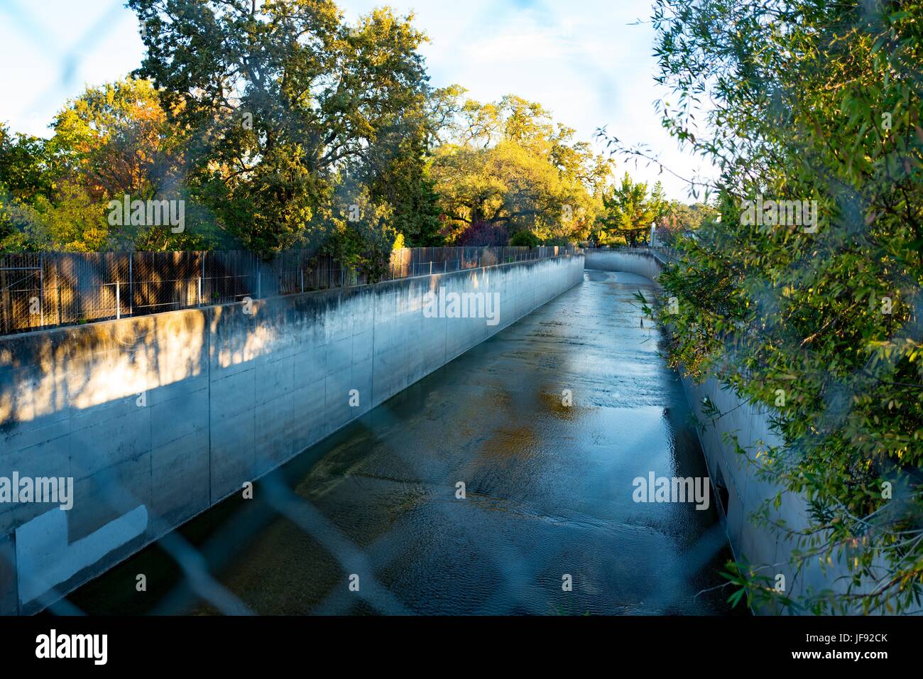 Un canal de agua de lluvia de hormigón es visible, con agua fluyendo a través de una valla chainlink, 19 de octubre de 2016. Foto de stock