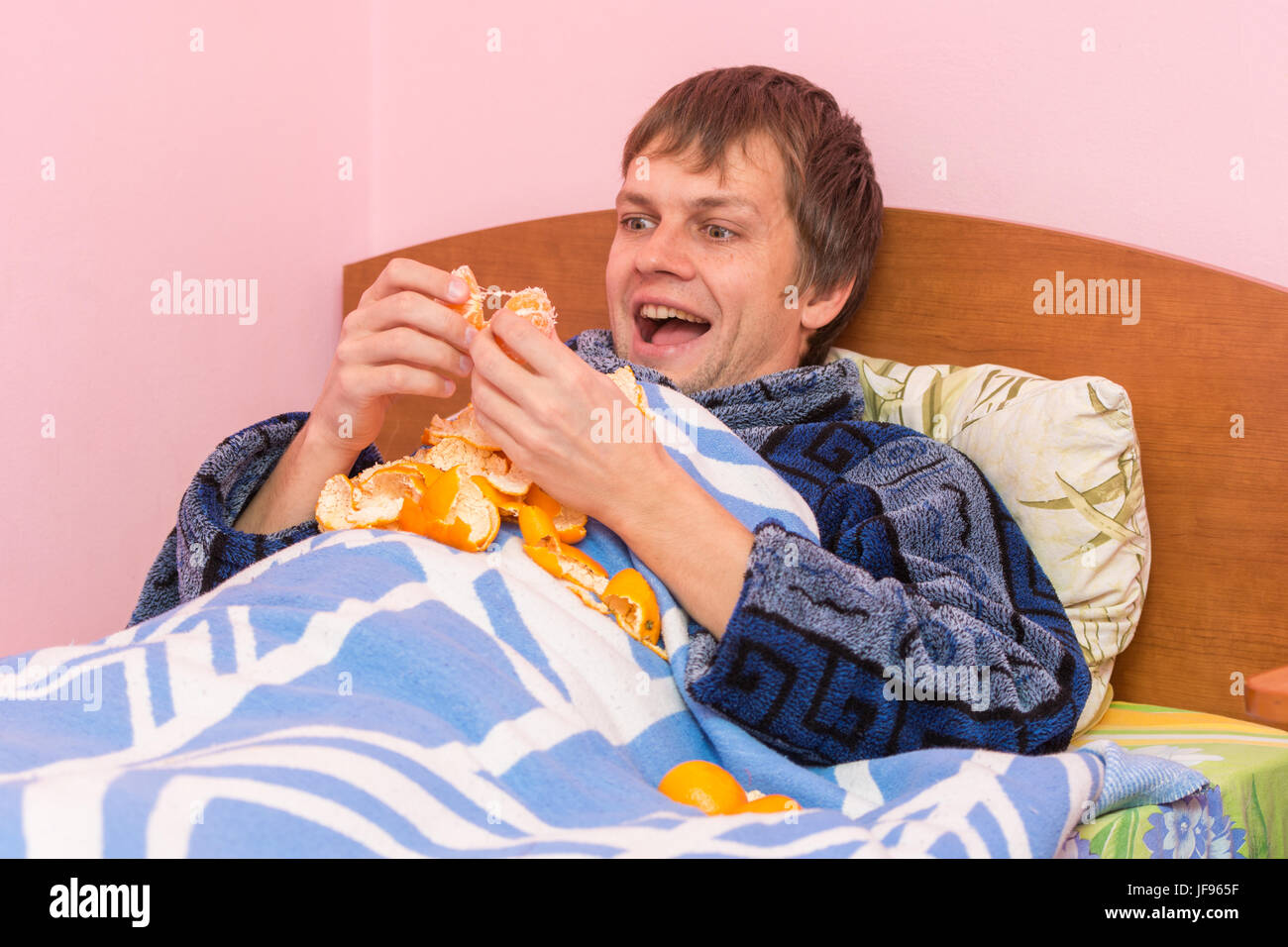 Hombre tumbado en la cama y comiendo mandarinas Foto de stock