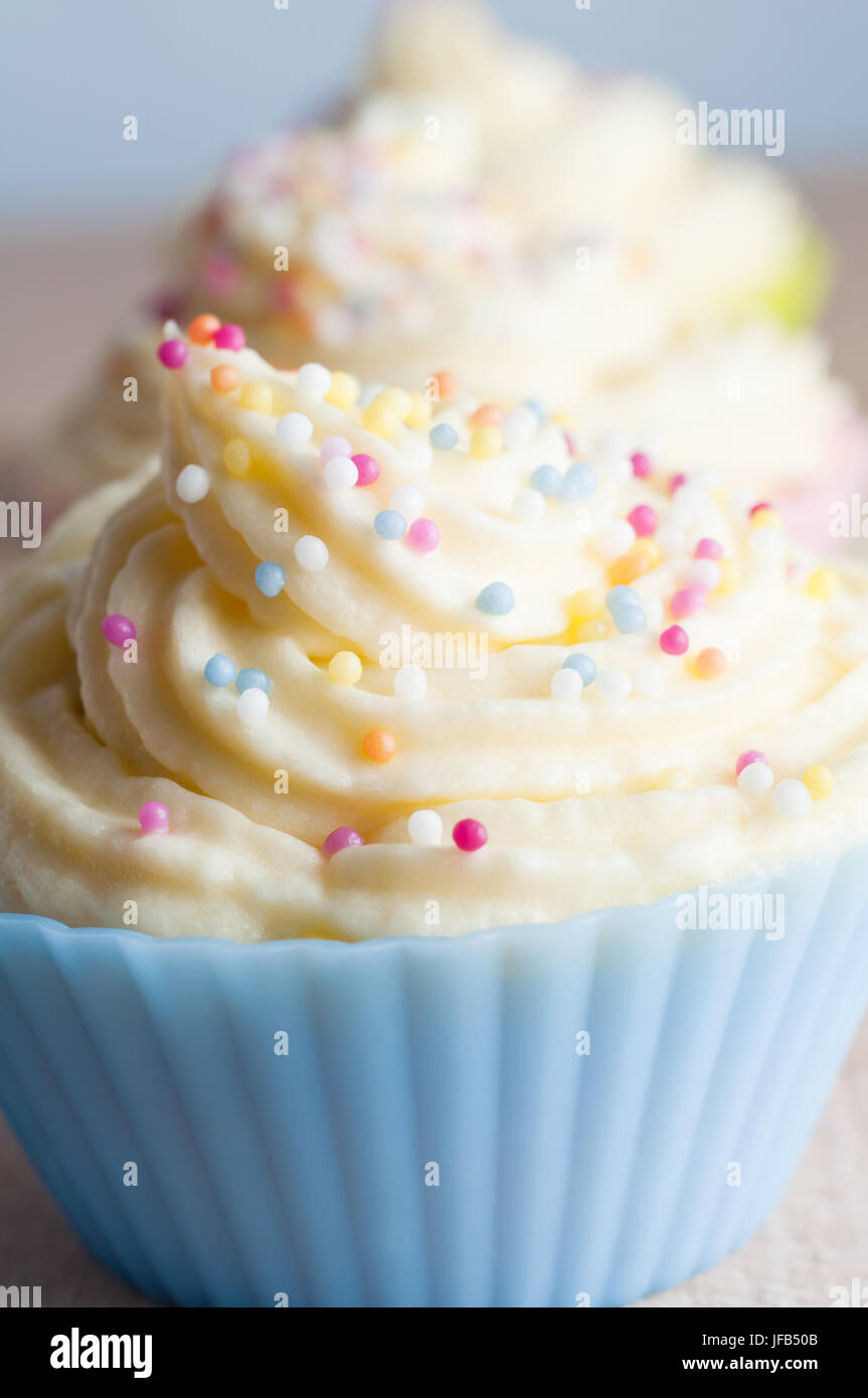 Cerca de Cup Cakes en una fila, decorado con espirales de buttercream color guinda y microgránulos esféricos, en los casos de color pastel. Foto de stock