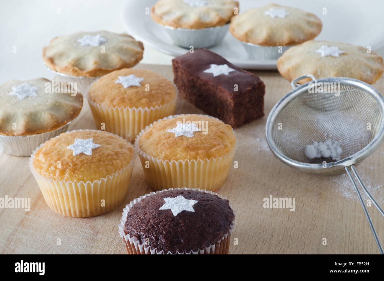Un grupo de Navidad tortas y pasteles de carne picada, decorado con formas de estrella de azúcar impalpable cernida, sobre una tabla de cortar de madera con la placa en el fondo, una Foto de stock