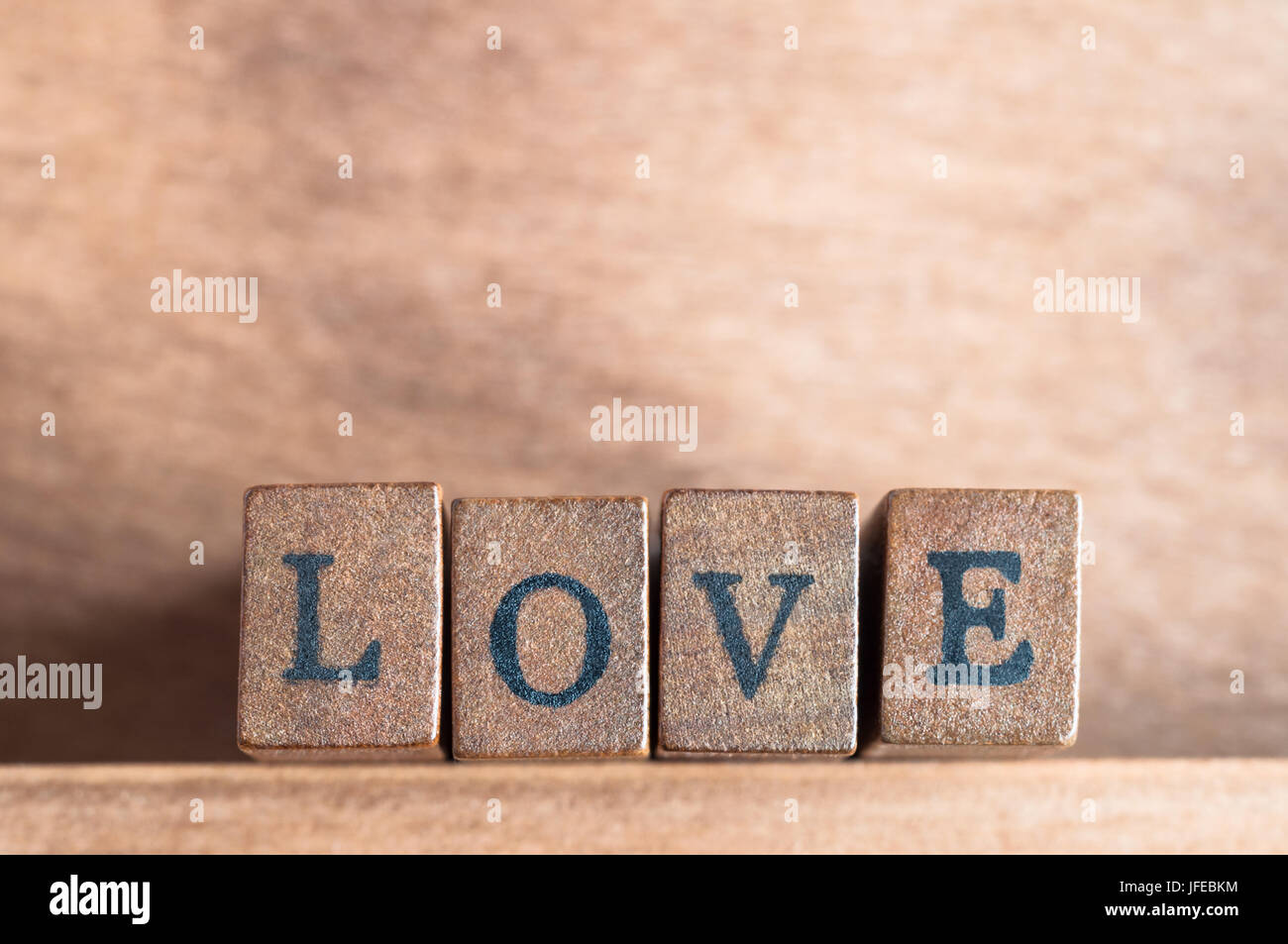 La palabra "amor" enunciadas en una fila de bloques de madera con letras vintage retro o apariencia, mirando hacia delante en un estante de madera con fondo de madera Foto de stock