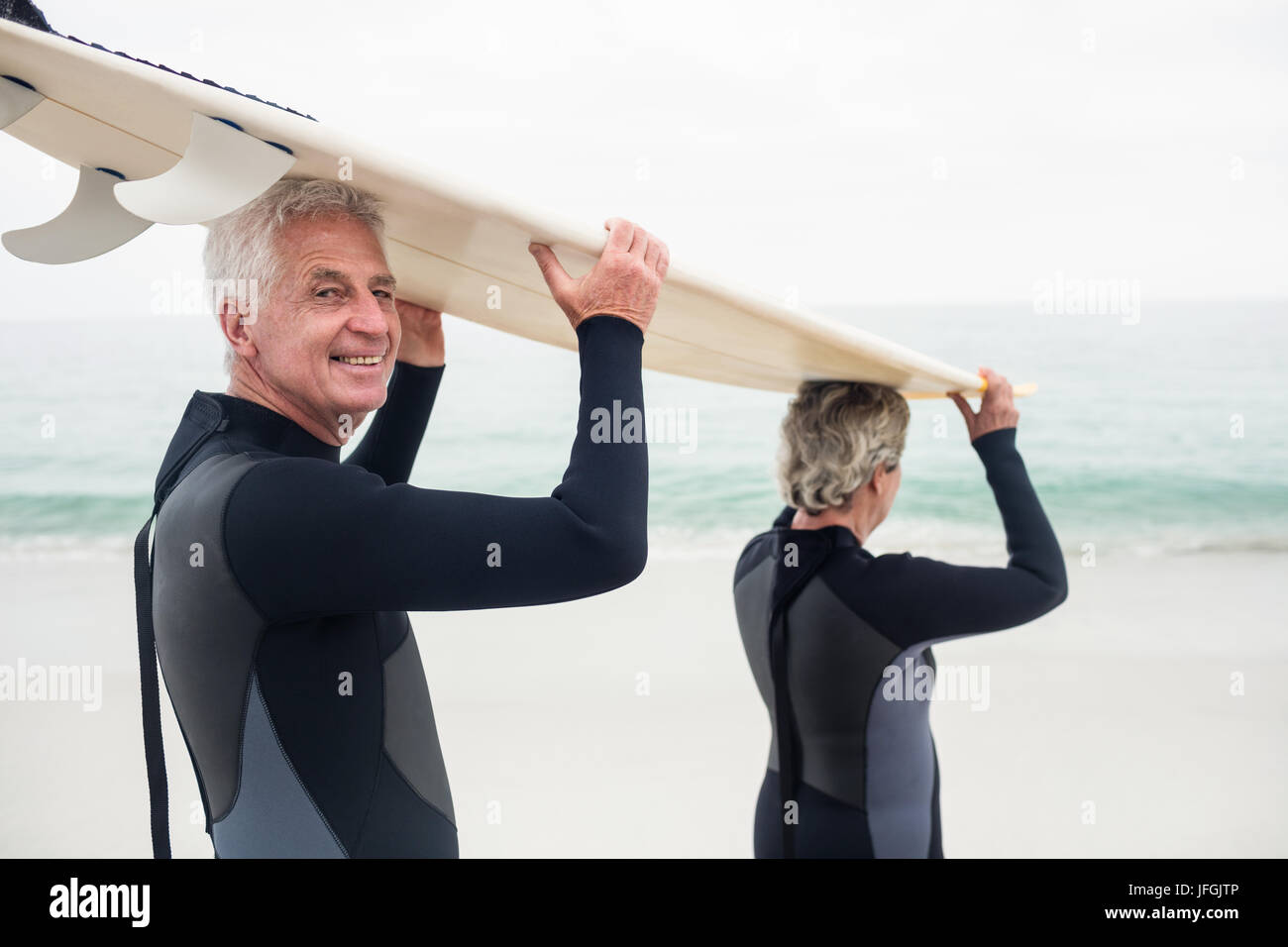 Las parejas ancianas en llevar traje de neopreno, tablas de surf sobre la cabeza Foto de stock