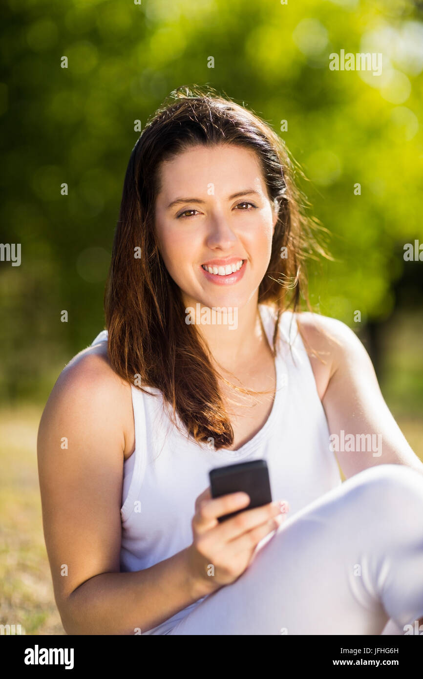 Mujer sentada sobre la hierba y a través de teléfono móvil Foto de stock