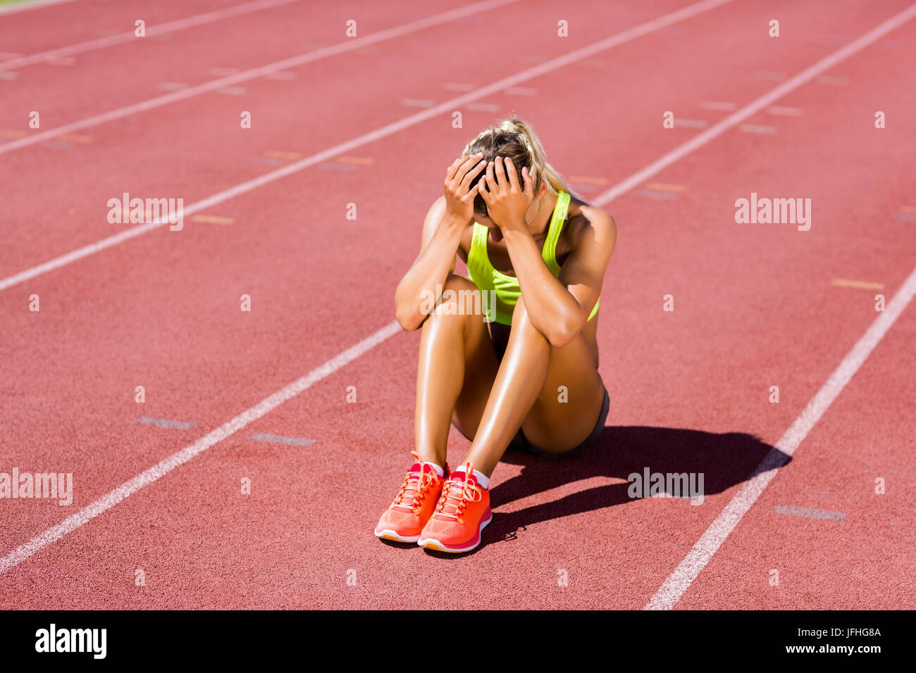 Malestar atleta femenina sentada sobre una pista de atletismo Foto de stock