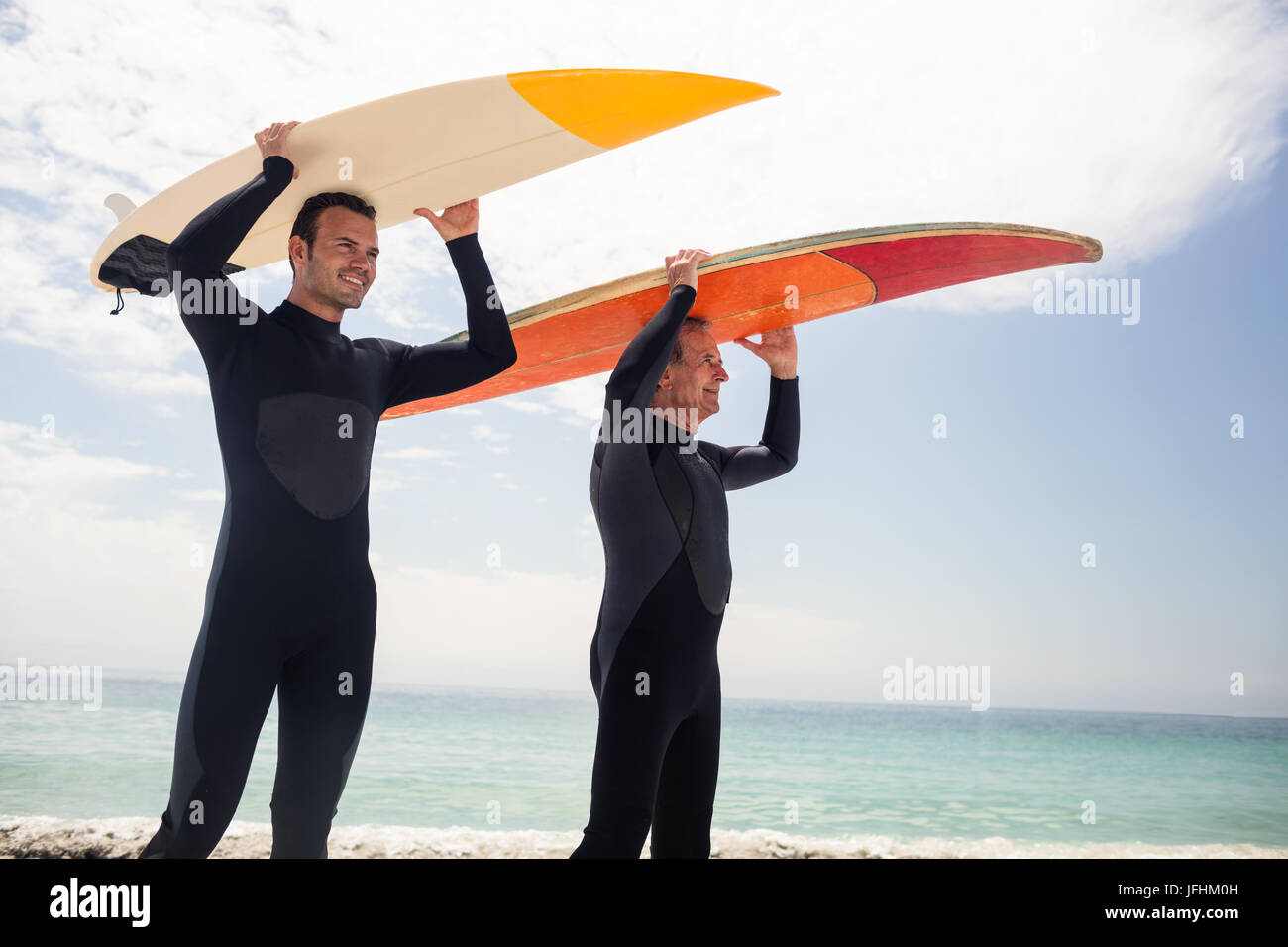 Padre e hijo feliz llevando una tabla de surf sobre su cabeza Foto de stock