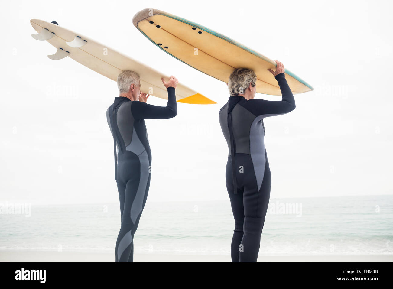 Las parejas ancianas en llevar traje de neopreno, tablas de surf sobre la cabeza Foto de stock