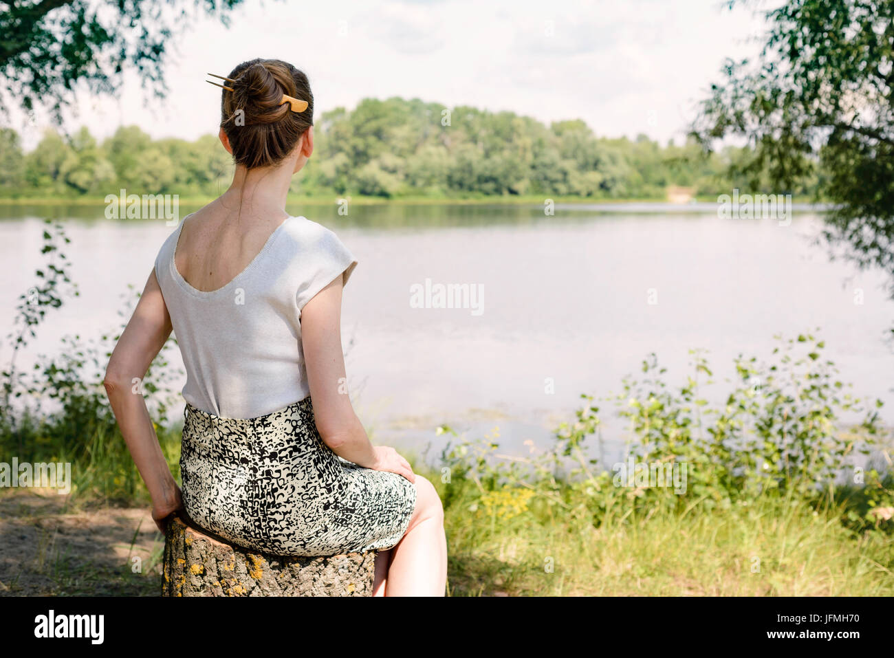 Una mujer está sentada cerca del río Dnieper, en Kiev, Ucrania, y está viendo u observando en la lejanía, bajo el cálido sol de verano y suave Foto de stock