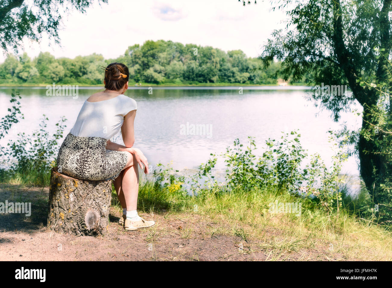 Una mujer está sentada cerca del río Dnieper, en Kiev, Ucrania. Ella es pensar mientras se está viendo u observando en la lejanía, en un ambiente cálido y suave Foto de stock