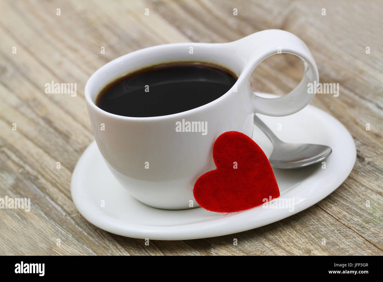 Taza de café negro en taza blanca y corazón rojo apoyado contra ella Foto de stock