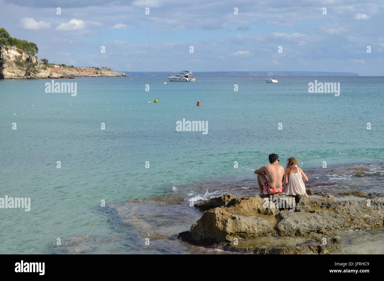 Chico y chica sentada sobre una roca de la playa Cala Mayor, en Palma de Mallorca, España Foto de stock