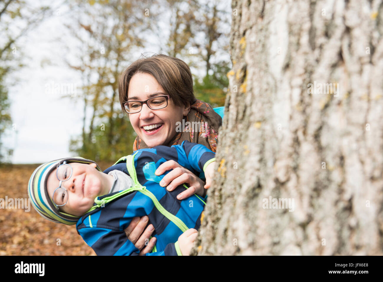 Madre e hijo peeking del gran árbol y riendo en el paisaje del otoño Foto de stock