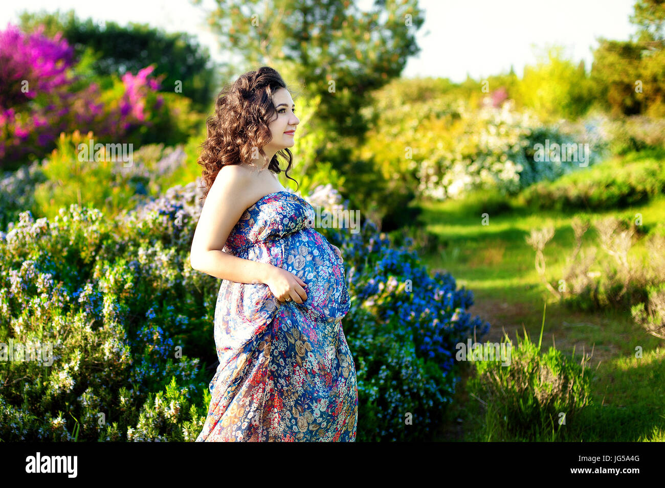 Bonita mujer embarazada posando en un verde jardín de romero Foto de stock