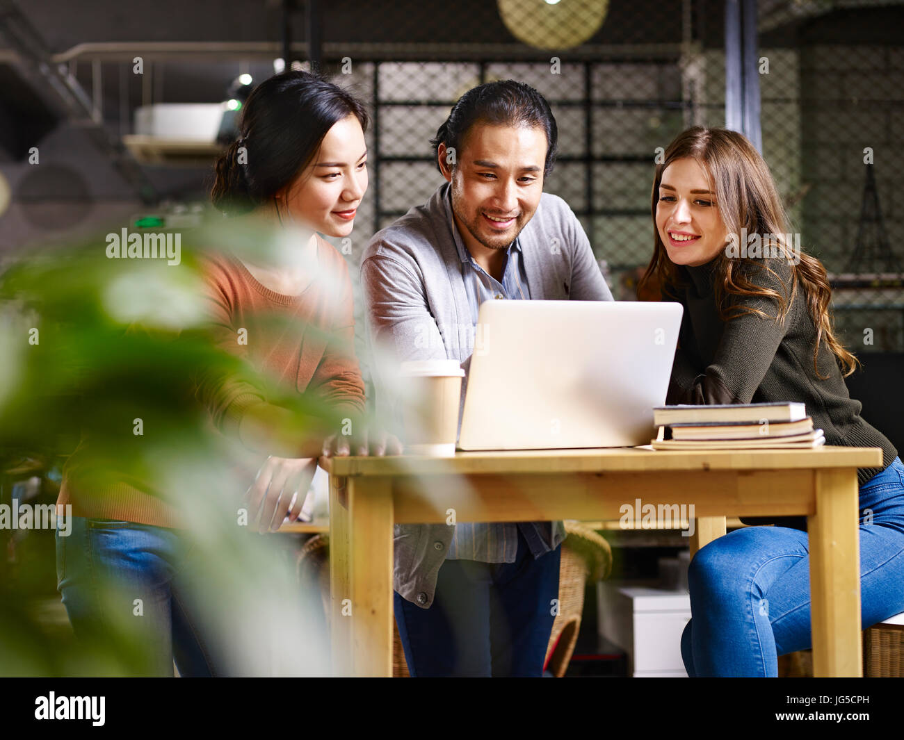 Un equipo de empresarios asiáticos y caucásicos trabajando juntos en Office mediante ordenador portátil. Foto de stock