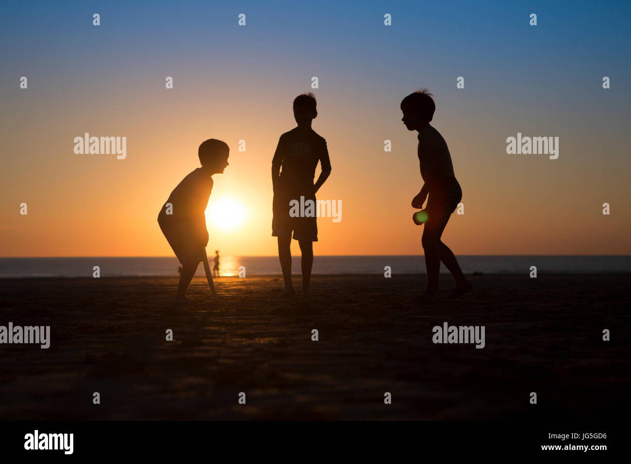 Niños jugando críquet en la playa cuando se pone el sol, Devon, Reino Unido Foto de stock