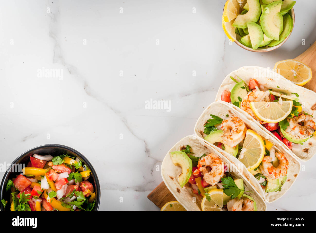 Los mariscos. La comida mexicana. Tacos de tortilla con salsa casera  tradicional ensalada fresca, perejil, limón, aguacate y gambas a la prenda.  En un mármol blanco Fotografía de stock - Alamy