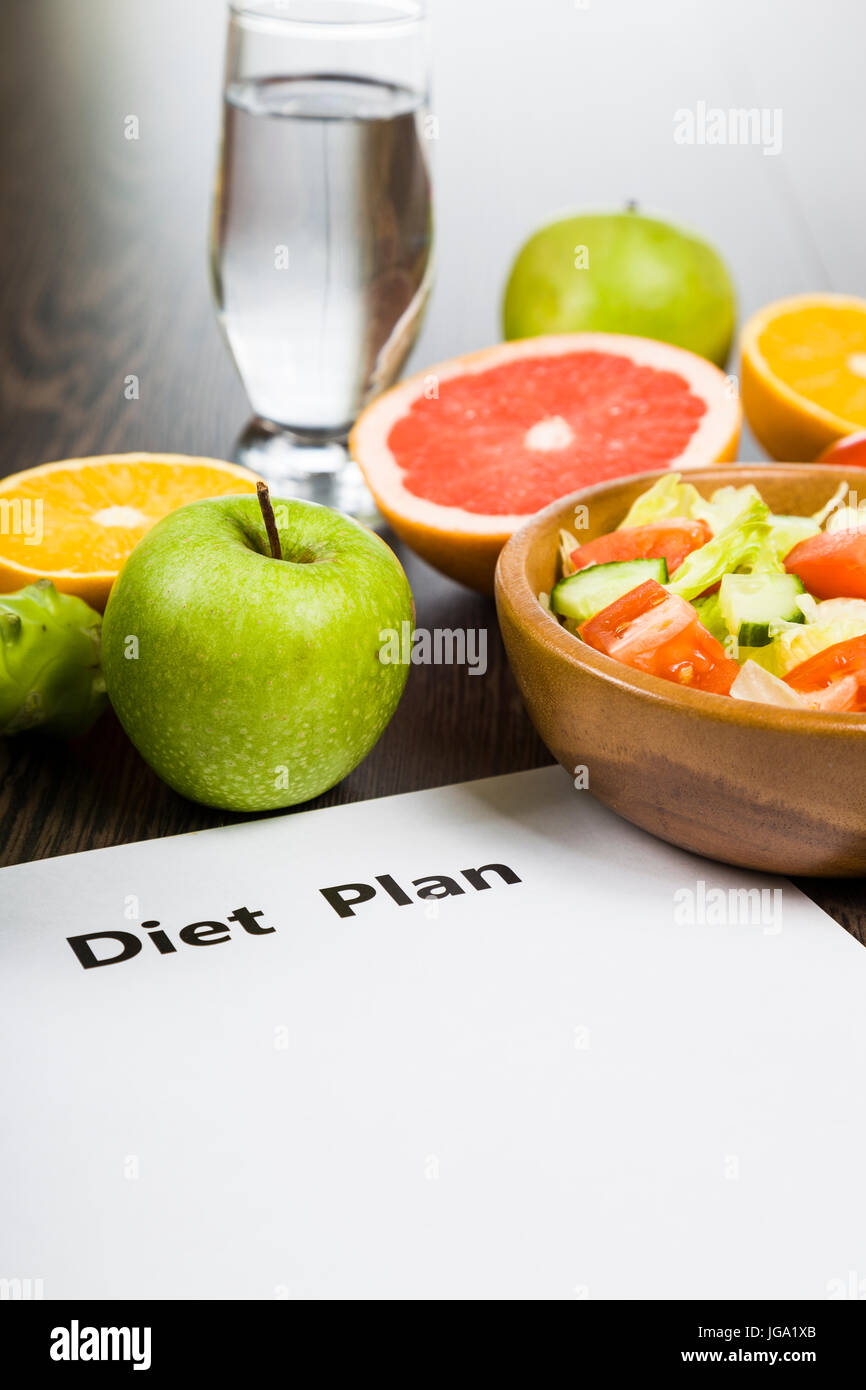 Los alimentos y la hoja de papel con un plan de dieta sobre una mesa de madera oscura. concepto de dieta y estilo de vida saludable. Foto de stock