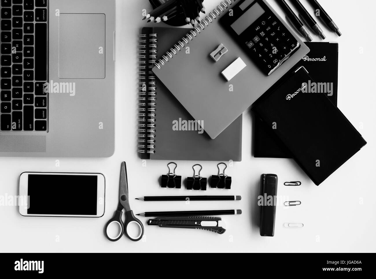Vista superior de suministros de oficina, teléfonos inteligentes y ordenadores portátiles en blanco y negro Foto de stock