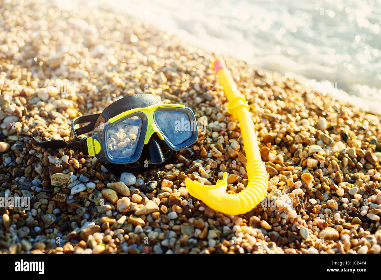 Una vista de gafas de natación y un tubo de snorkel tumbado en la arena cerca del agua en una playa soleada. Foto de stock
