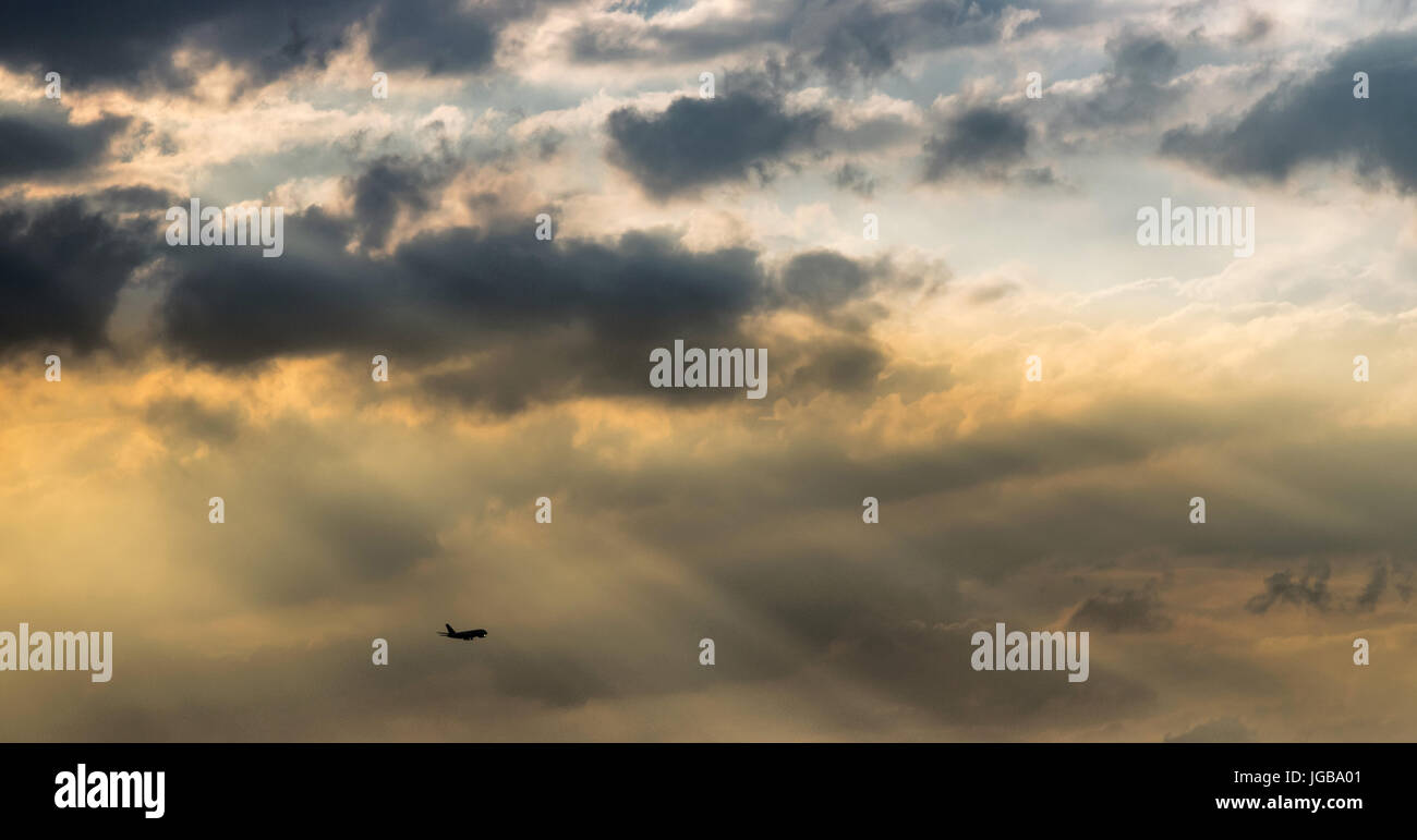 Silueta de avión sobrevolando el atardecer y ejes de luz, nublado y cielo nublado, hermosa cloudscape Foto de stock