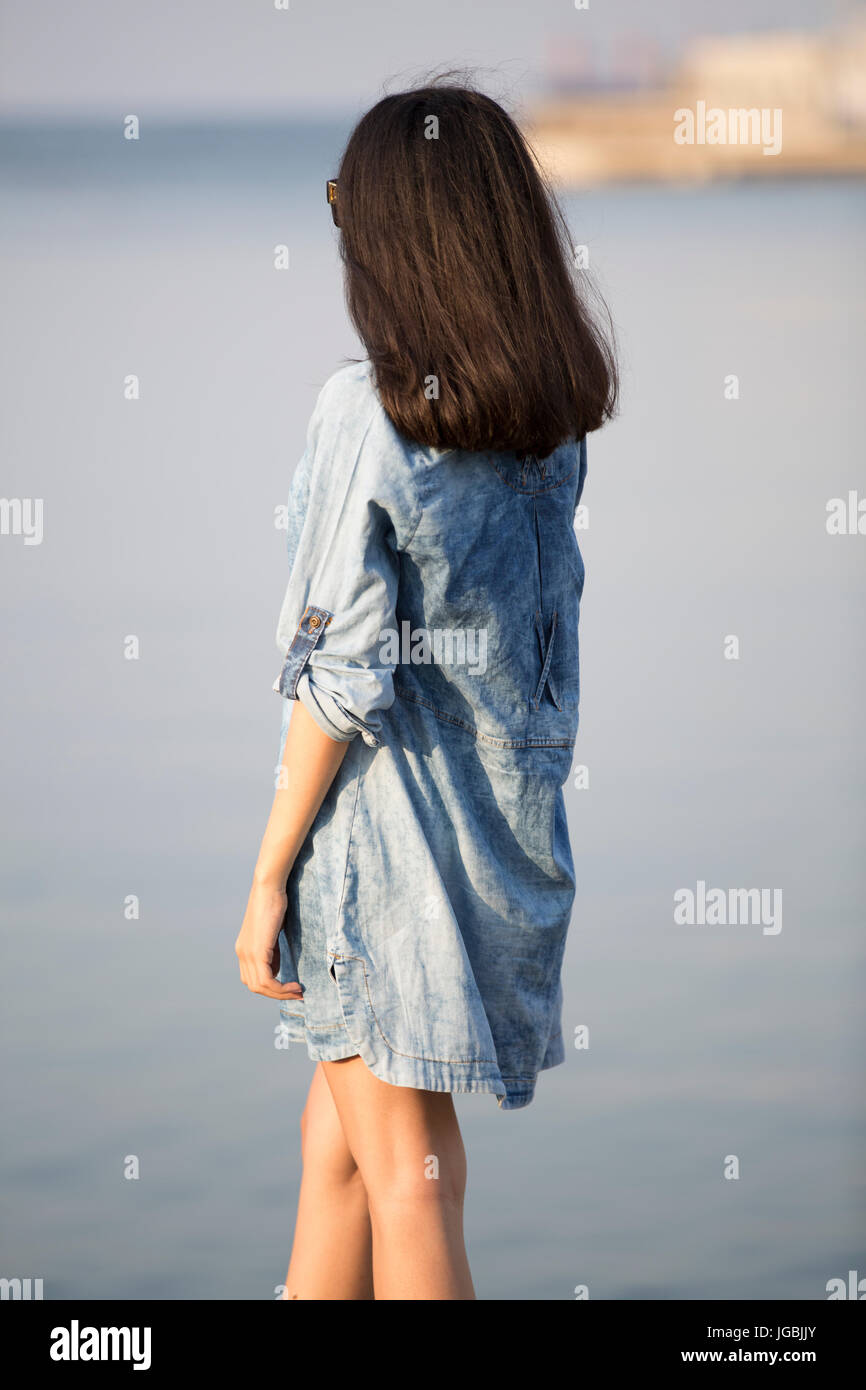 Vista trasera de una mujer joven llevaba un vestido de verano azul por el mar permanente Foto de stock