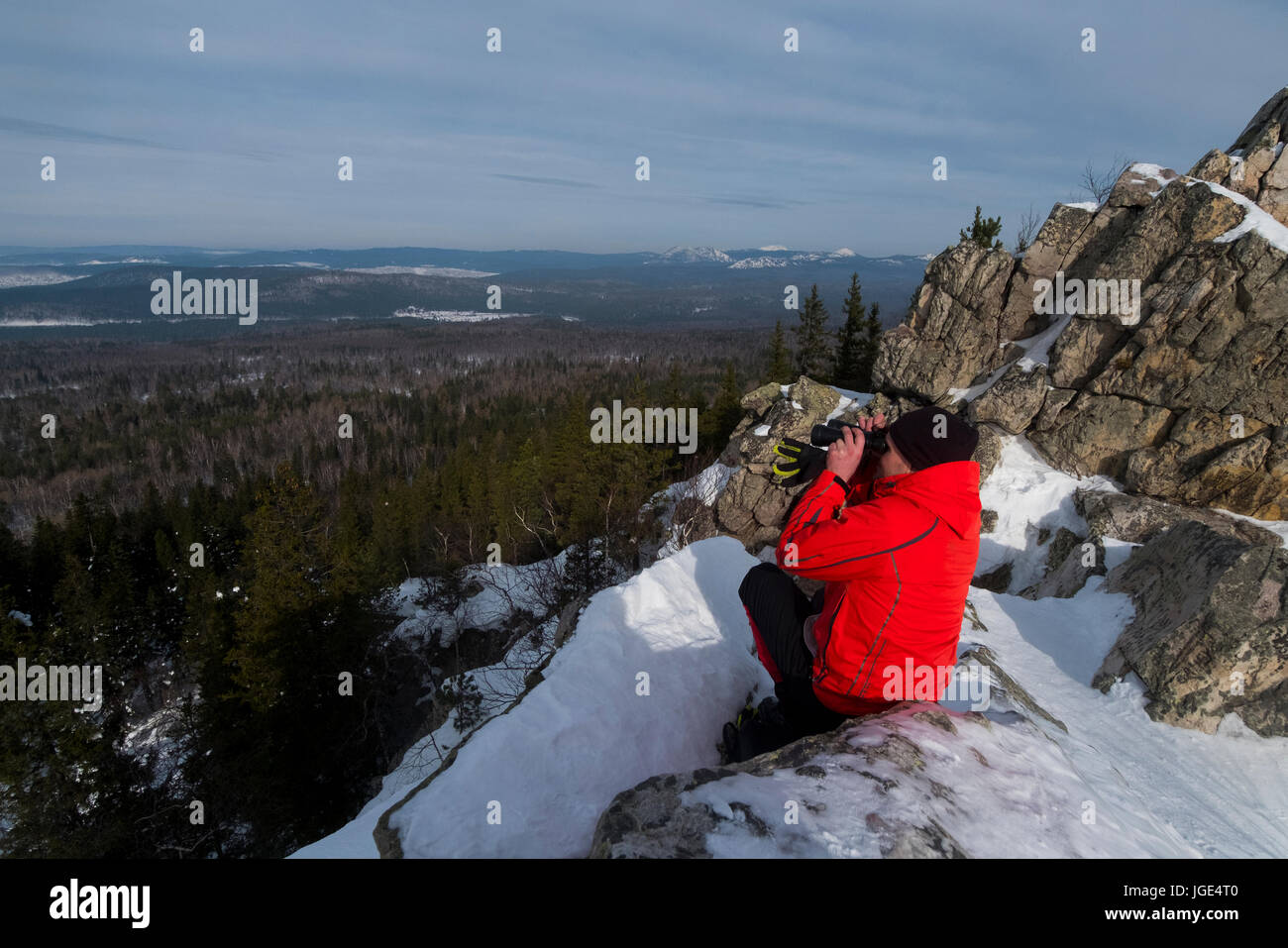 Caucasian hombre sentado en la nieve, admirando vistas panorámicas del bosque Foto de stock