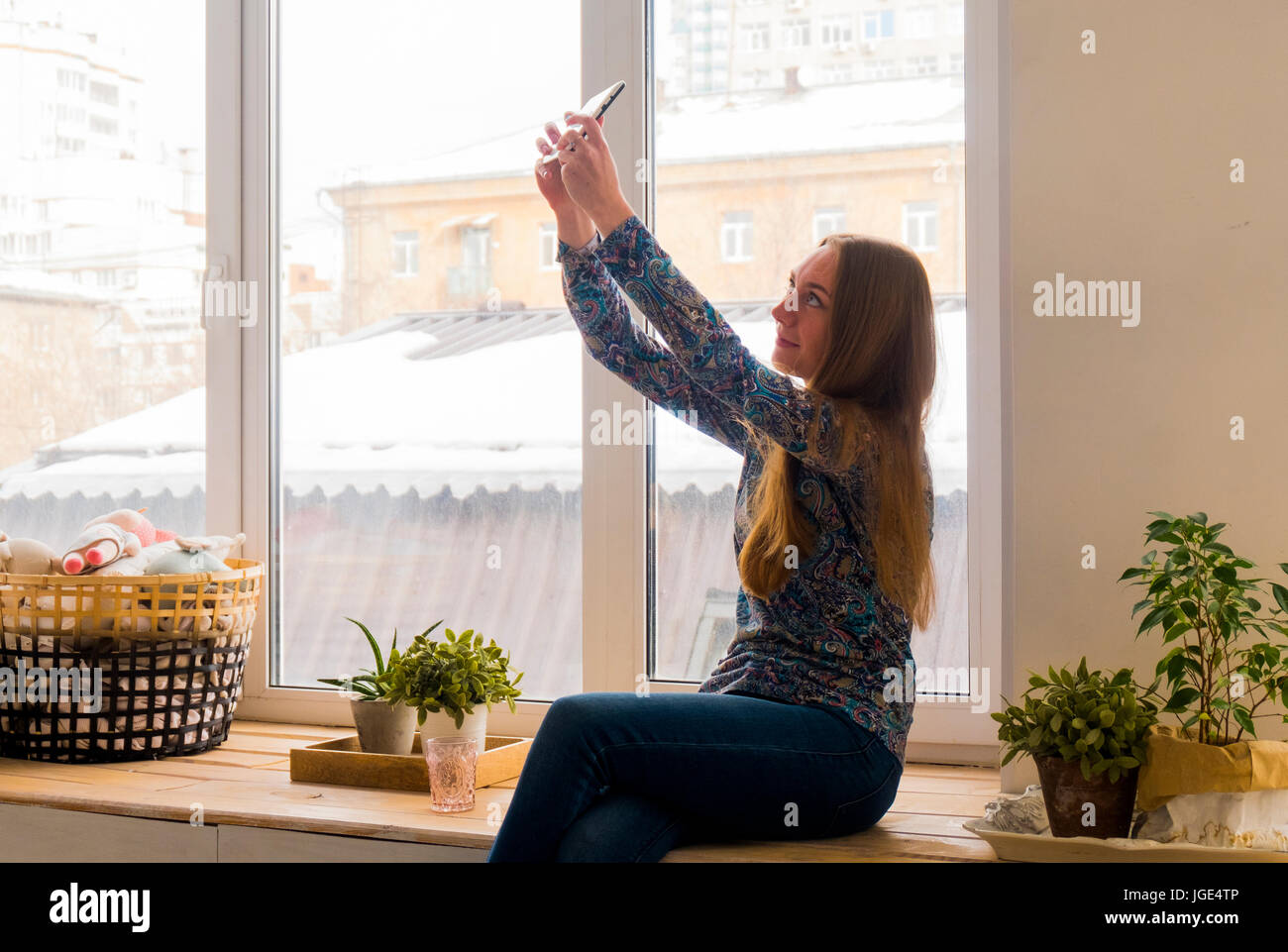 Mujer caucásica sentado en la ventana posando para teléfono celular selfie Foto de stock