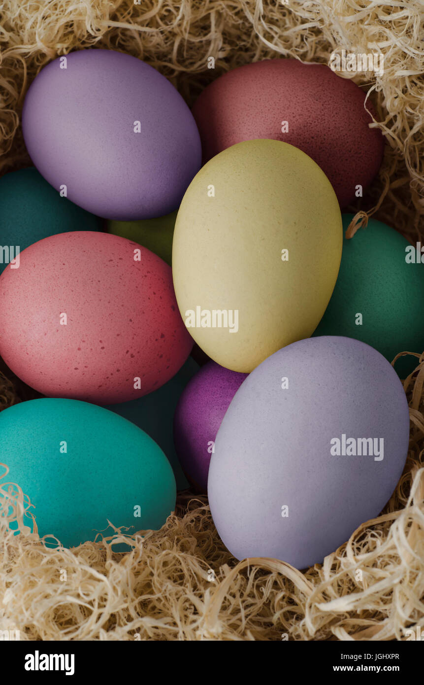 Vista elevada de huevos de Pascua pintados en distintas tonalidades, agrupados y anidado en césped seco. Foto de stock