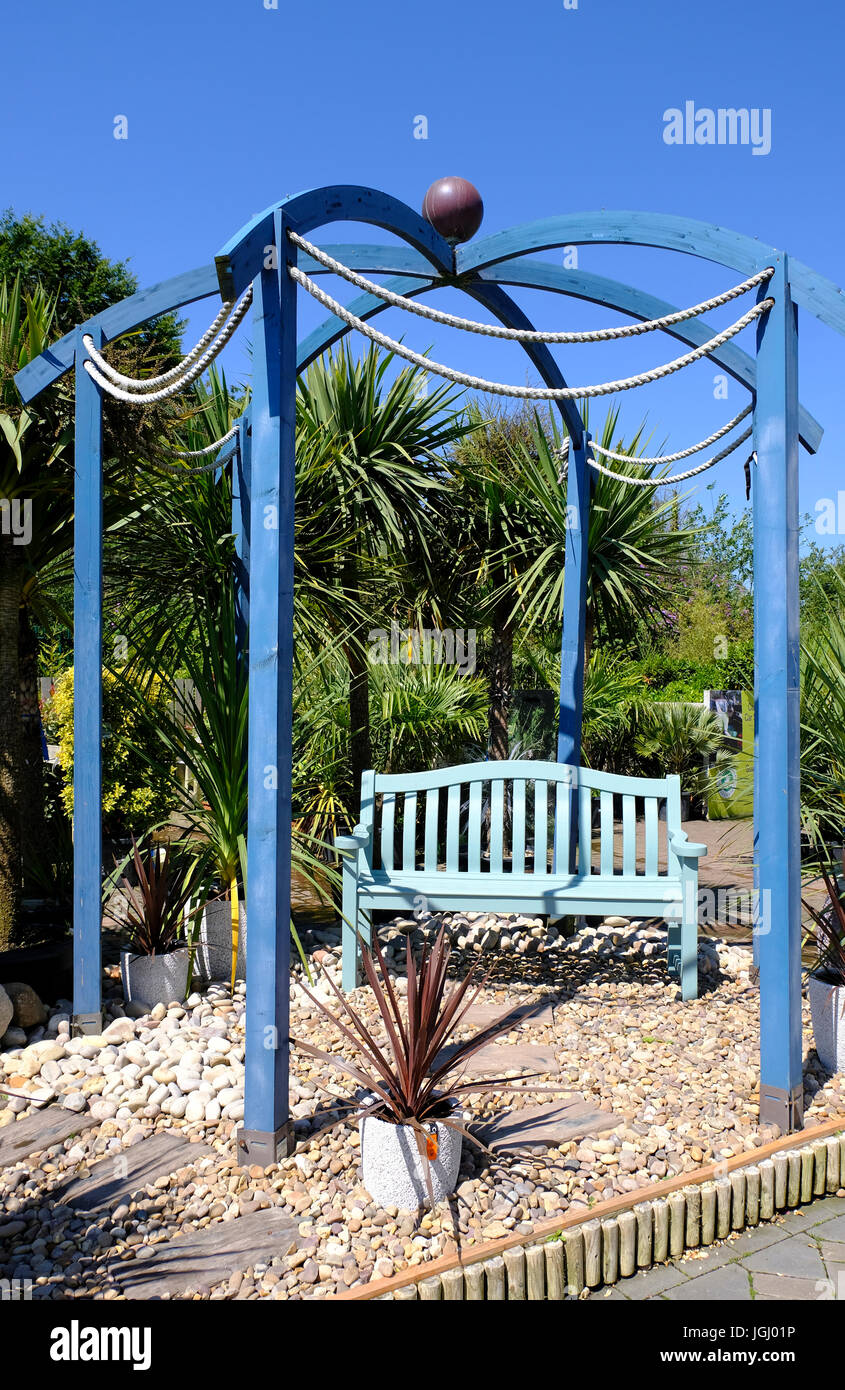 Asiento de jardín de madera pintada de azul bajo el cenador azul en venta en centro de jardinería británica Foto de stock