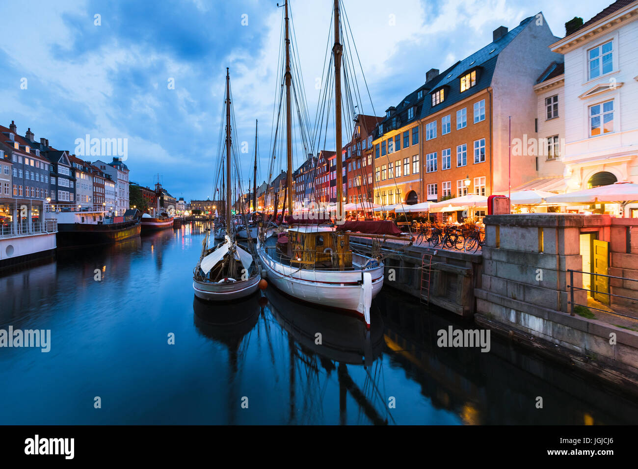 Copenhague Nyhavn (puerto nuevo) distrito con las luces de la ciudad después del atardecer durante la hora azul con barco velero y restaurantes, Dinamarca Foto de stock