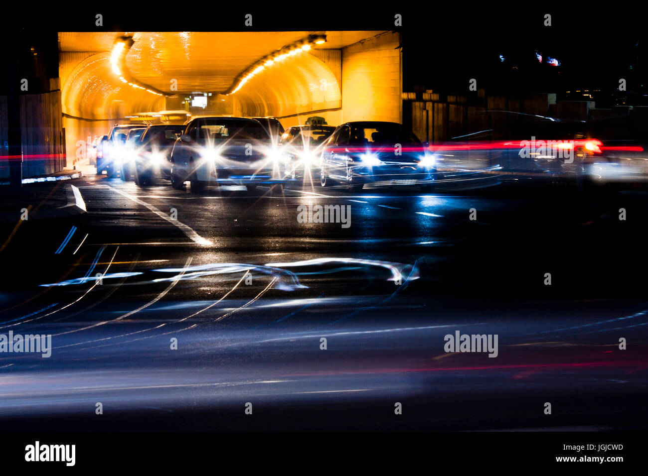 Tráfico nocturno en las calles de la ciudad. Coches en cola de espera a la salida del túnel en la intersección durante la conducción de vehículos en movimiento pasado dejando estelas de luz de color Foto de stock