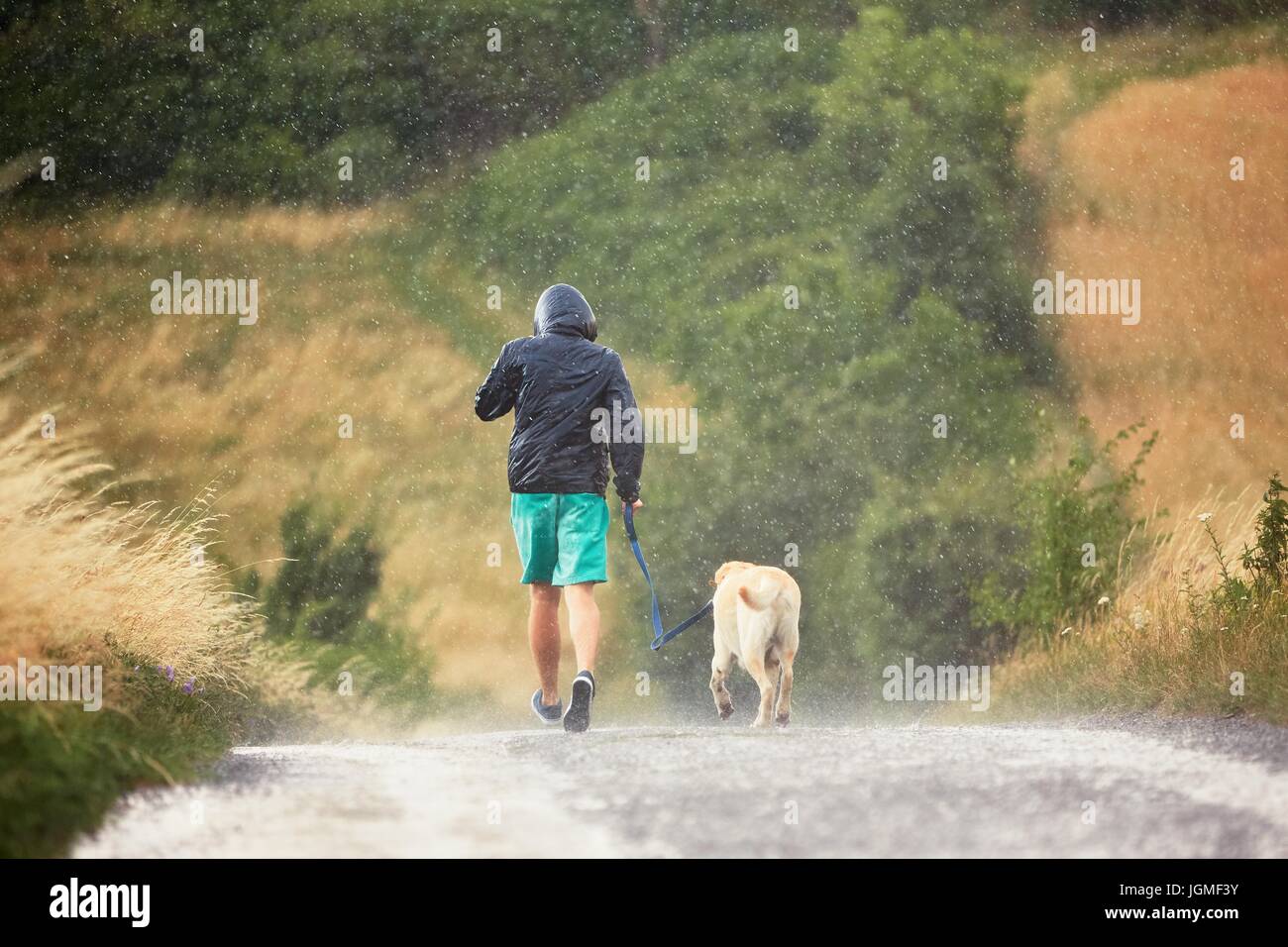 Joven corriendo con su perro (labrador retriever) en Heavy Rain en la carretera rural. Foto de stock