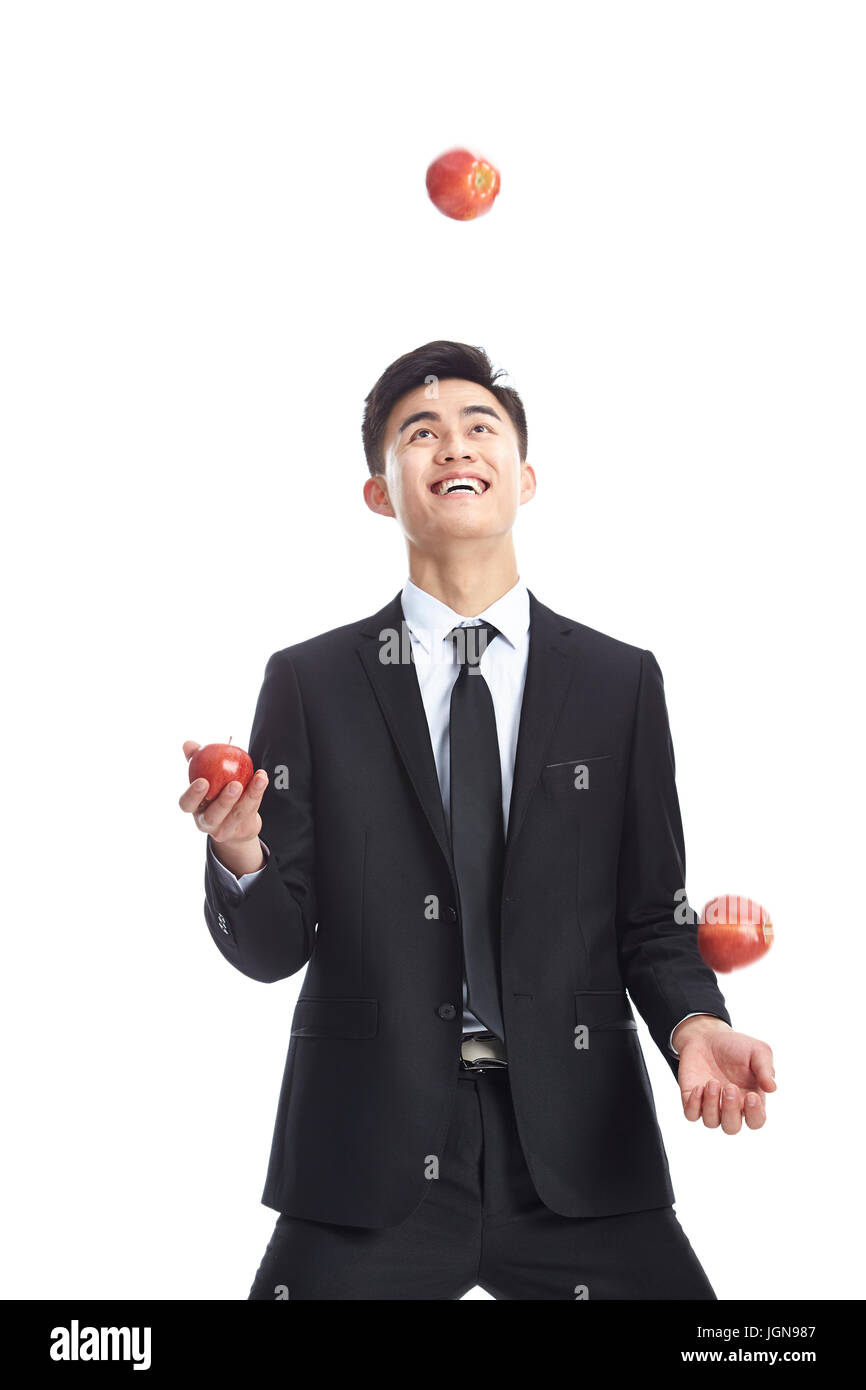 El hombre de negocios joven asiático vestidos de traje y corbata malabarismos con tres manzanas, aislado sobre fondo blanco. Foto de stock