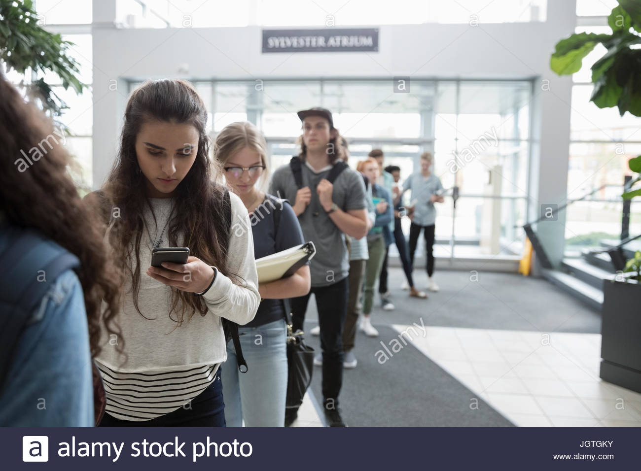 Estudiante Universitario femenino texto con teléfono celular en cola. Foto de stock