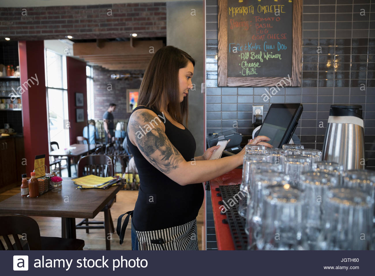Embarazada tatuado camarera utilizando el ordenador, introducir orden en el restaurante Foto de stock