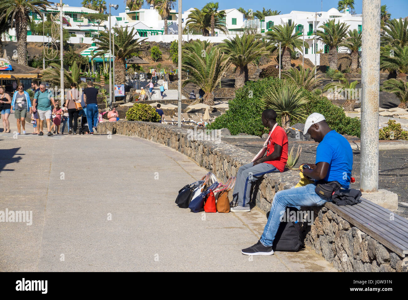Afrikanische Handtaschen und Armbanduhren Strassenhaendler mit der beim Badestrand un paseo de la Playa de Las Cucharas, Costa Teguise, Lanzarote, Kanar Foto de stock