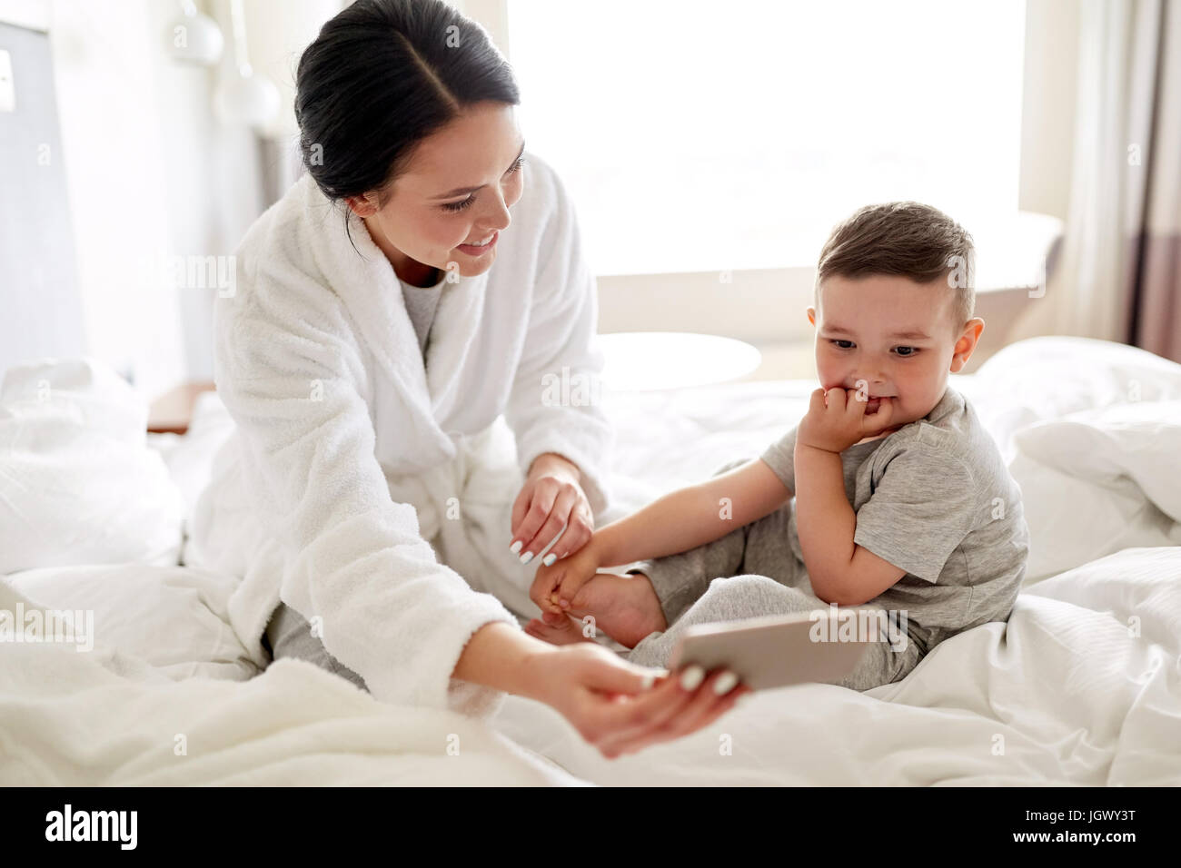 Subir y bajar Derecho cilindro Madre e hijo con el smartphone en la cama en el hotel Fotografía de stock -  Alamy