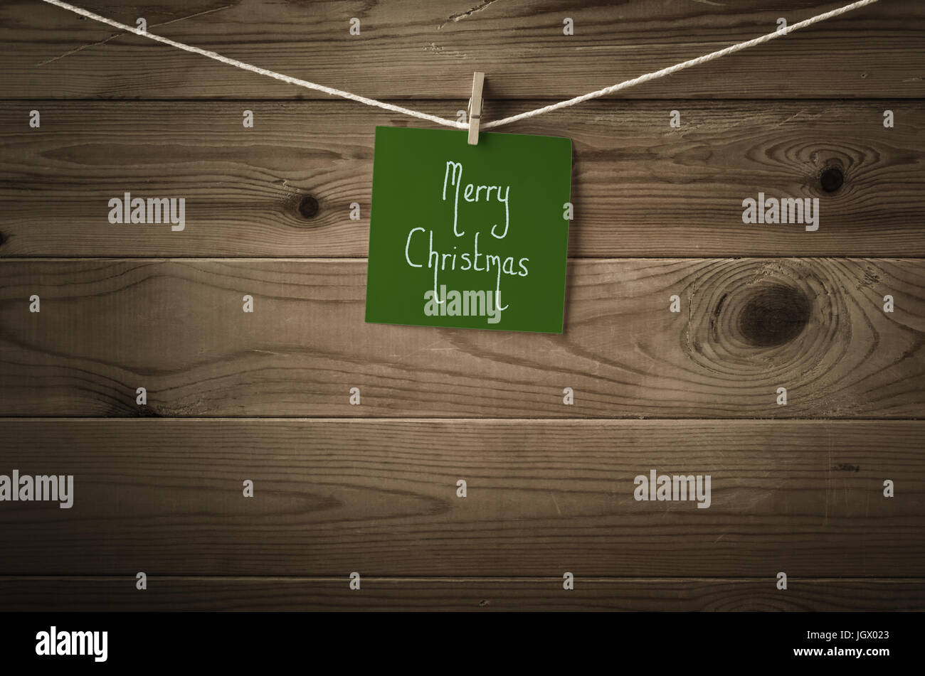 Feliz Navidad mensaje escrito sobre un cuadrado de papel nota verde oscuro festiva y vinculada a una cadena de línea de lavado, valla de madera de fondo. Retro Foto de stock