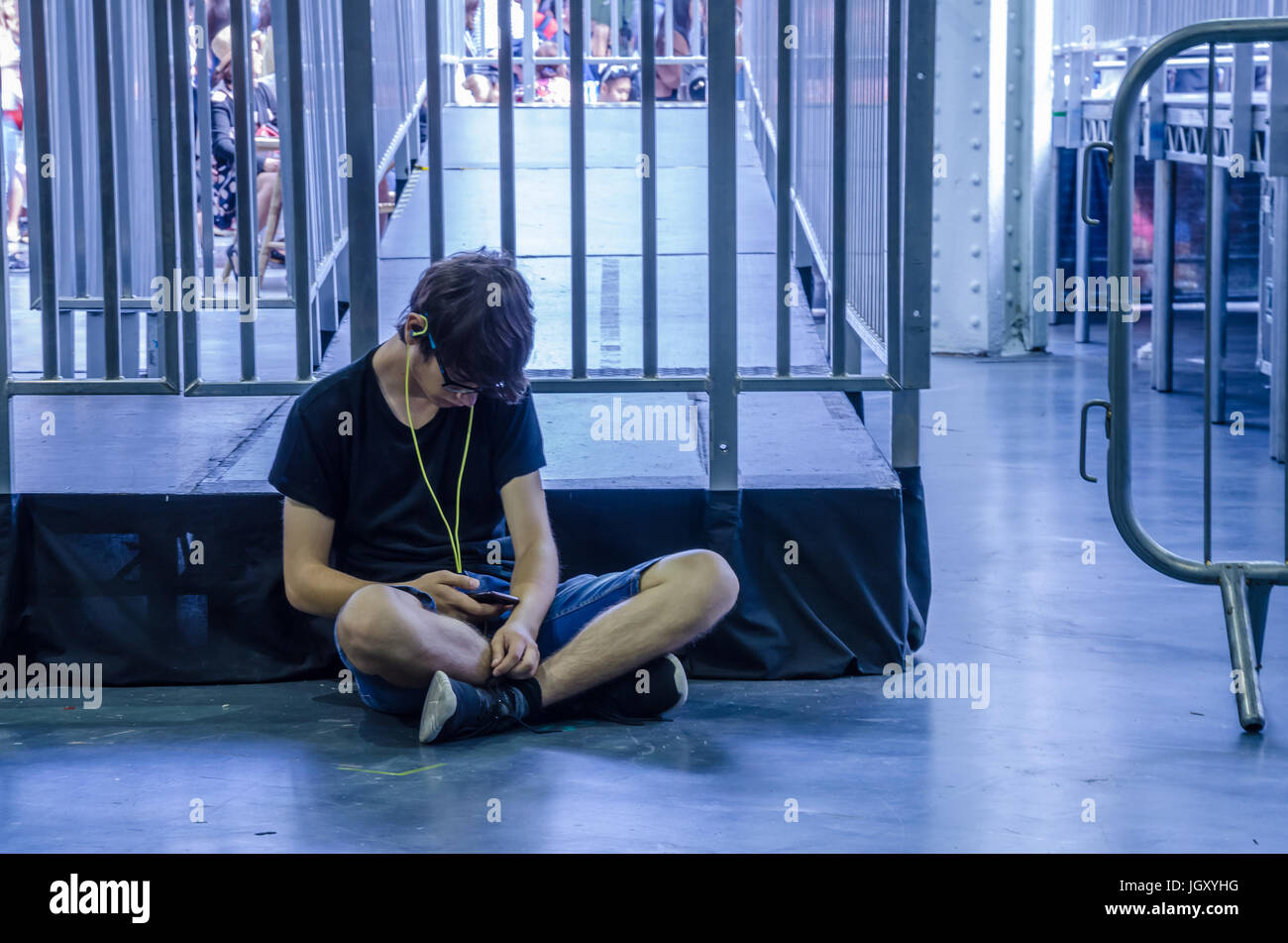 Un adulto joven sentada sola en el piso listado de música en un teléfono móvil. Foto de stock