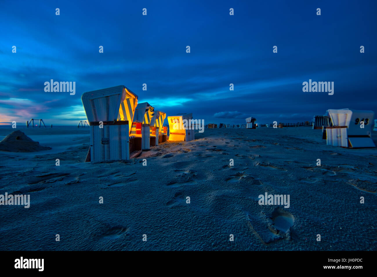 Crepúsculo en la playa de hundió Peter Ording en el norte de Alemania. Sillas de playa están iluminadas por luces suaves durante la tormentosa puesta de sol Foto de stock