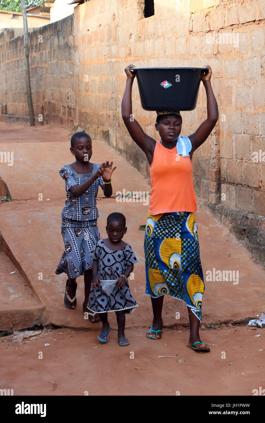 La vida del pueblo africano. Lata de agua. Muchacha africana llevando una cuenca de agua en la cabeza. Togoville. Togo. Foto de stock