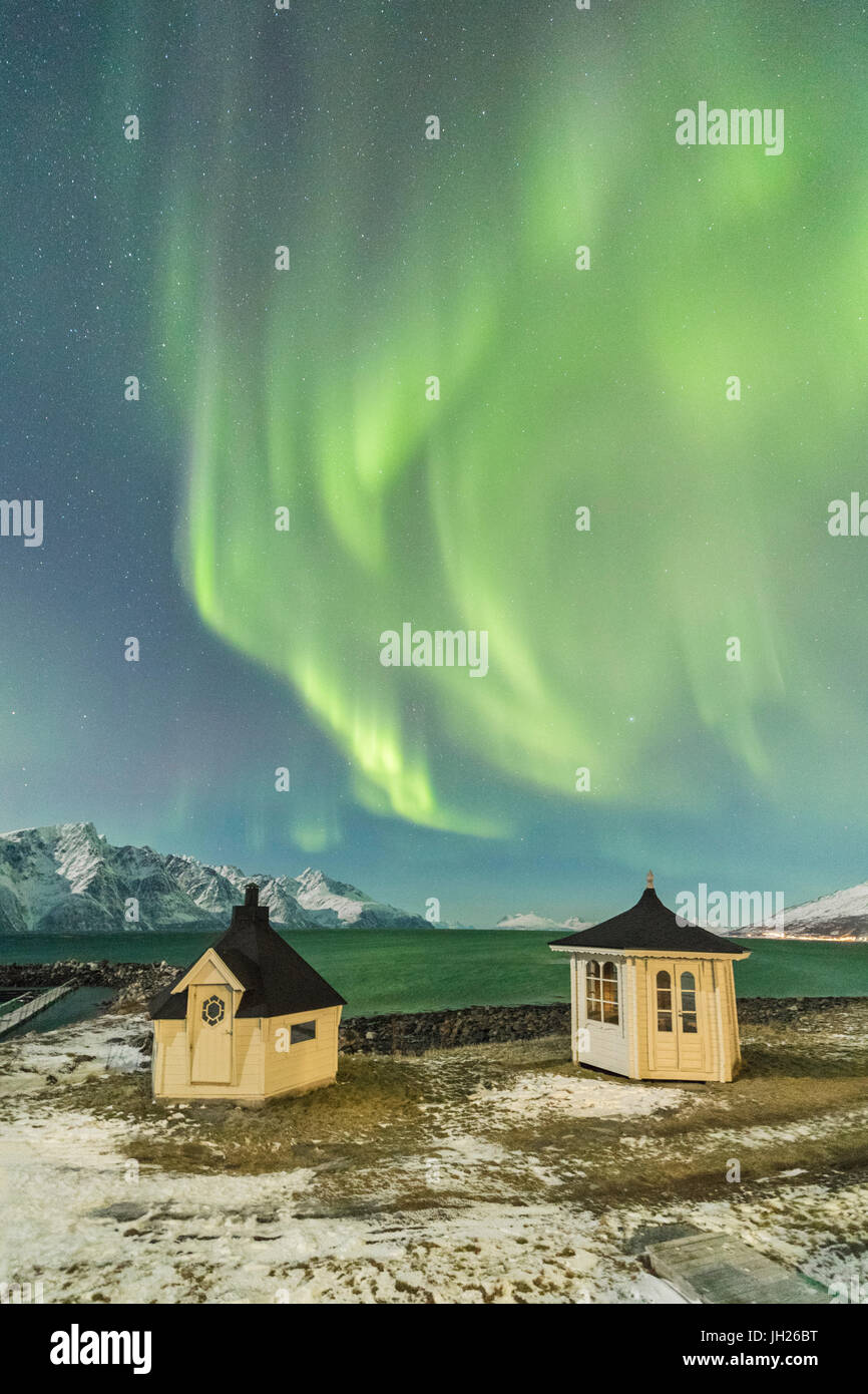 Las luces del norte y las estrellas iluminan las chozas de madera por el mar helado, Djupvik, Lyngen Alpes, Troms, Noruega Foto de stock